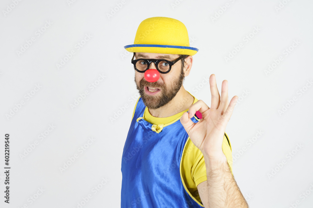 A clown in a bright blue and yellow suit, glasses and a hat shows an OK gesture A clown in a bright blue and yellow suit, glasses and a hat shows an OK gesture