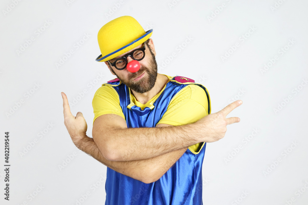 A clown in a bright blue and yellow suit hugs himself and shows hand gestures