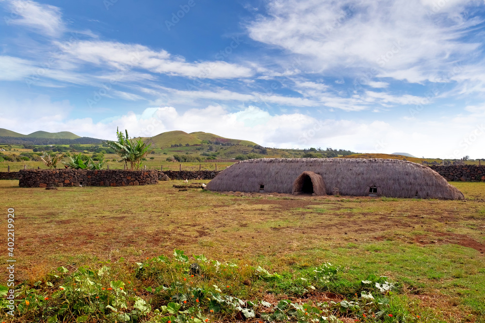 Obraz premium Old Rapa Nui thatch-roofed house at the ceremonial center of Vaihu, on Easer Island, against a blue sky covered by white clouds.
