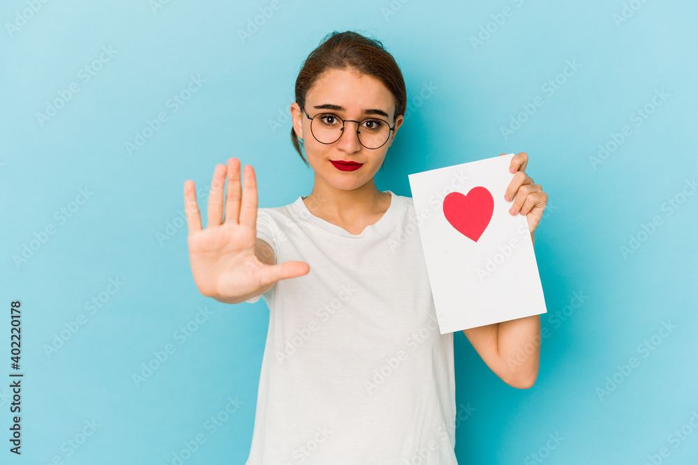 Young skinny arab girl holding a valentines day card standing with outstretched hand showing stop sign, preventing you. Young skinny arab girl holding a valentines day card standing with outstretched hand showing stop sign, preventing you.