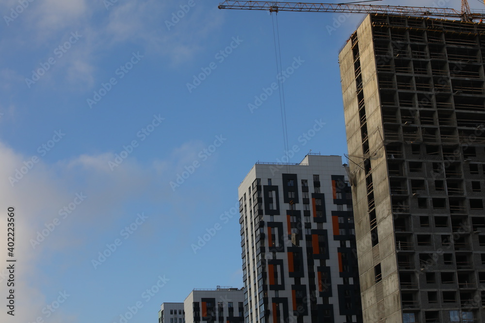 Construction of a new house.Unfinished building concrete gray structure many floors windows without glass and a crane on the background of a new white housing with a beautiful finish on the facade