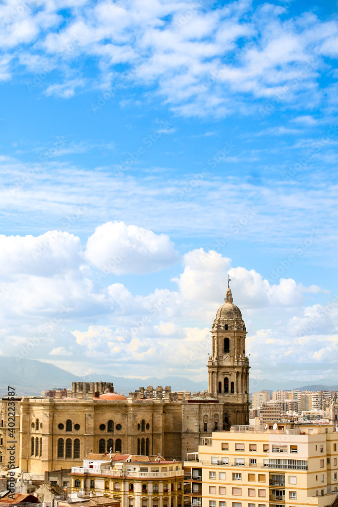 An aerial view of Malaga's skyline featuring Malaga Cathedral, with a blue cloudy sky as a backdrop.  Image has copy space.