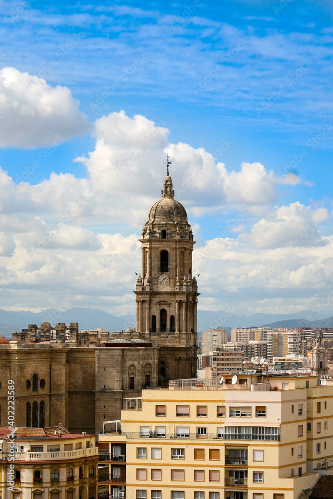A view of Malaga's skyline featuring Malaga Cathedral, with a blue cloudy sky as a backdrop.  Image has copy space.
