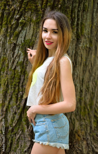 Beautiful young girl standing by an old big tree in the Park