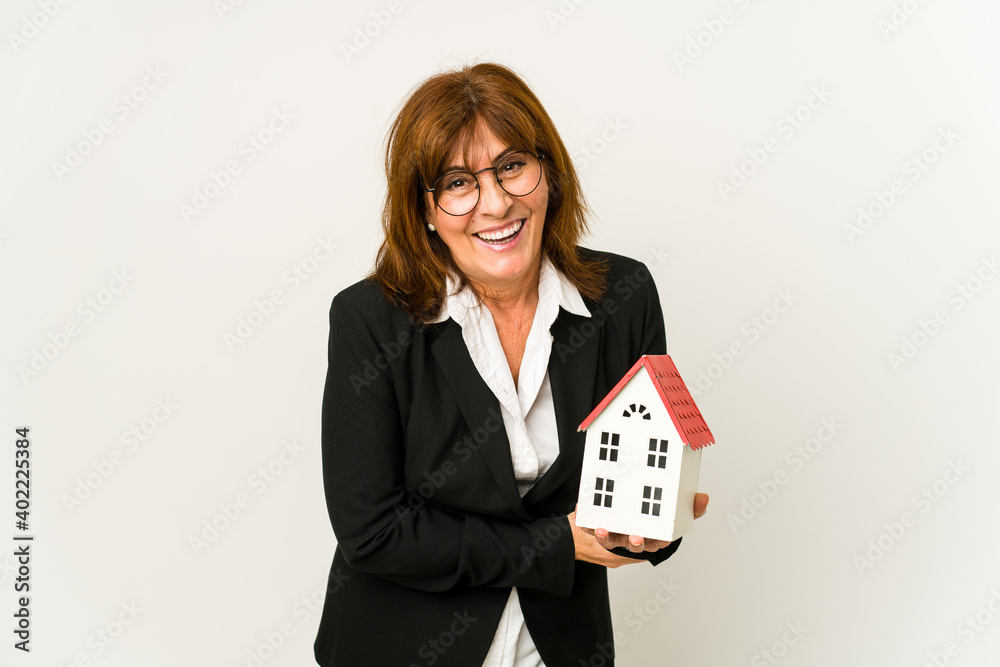 Middle aged real estate agent holding a house model isolated laughing and having fun. Middle aged real estate agent holding a house model isolated laughing and having fun.