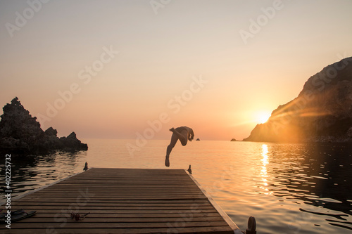 Silhouette of a man turned from behind while diving from a small marina on the sea. breathtaking sunset, golden hour.
