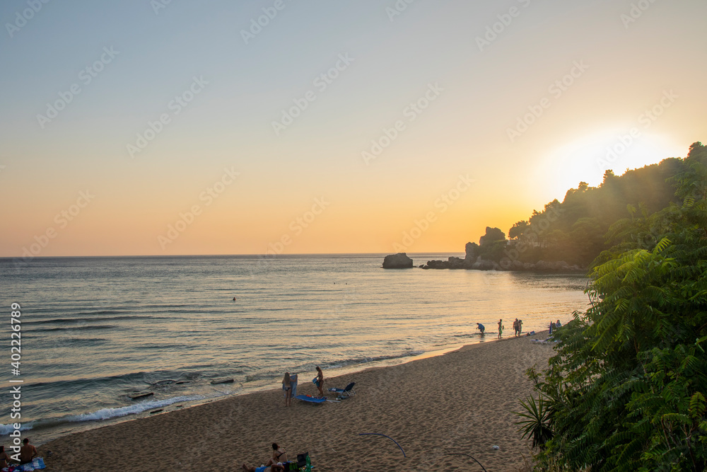 Sunset/sunrise over the sea with some rocks: shot in warm colors. Sandy beach without people, relaxing and romantic scenery, an unspoiled paradise. In Glyfada Beach, Corfu Sunset/sunrise over the sea with some rocks: shot in warm colors. Sandy beach without people, relaxing and romantic scenery, an unspoiled paradise. In Glyfada Beach, Corfu