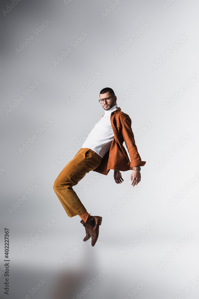 Fashionable man in eyeglasses and casual clothes posing on grey background