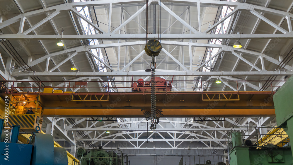 Fototapeta premium Yellow overhead crane with linear traverse and hooks in engineering plant shop. Industry concept.