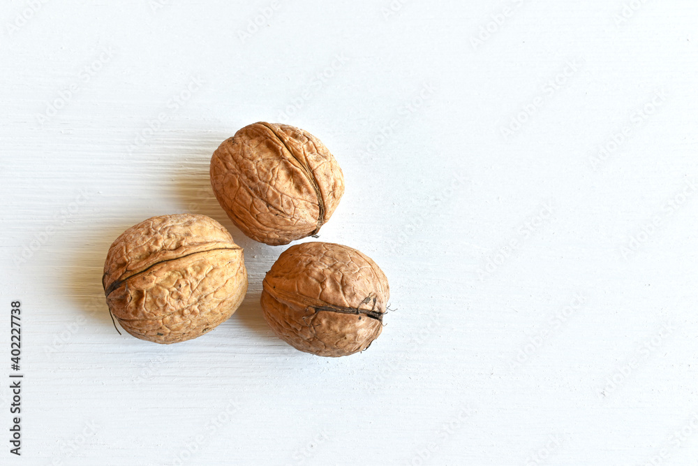 Walnuts (Juglans regia) in shell on white wooden background, close-up, top view. Walnuts (Juglans regia) in shell on white wooden background, close-up, top view.