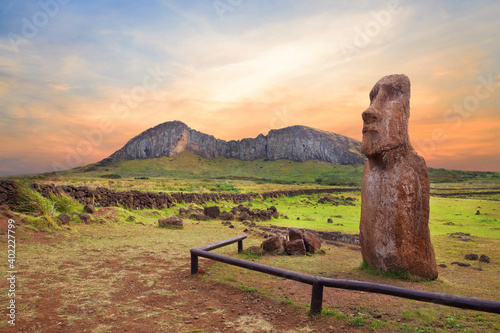 Stone fence and Moai statues at the entrance in the Ahu Tongariki ceremonial center on Easter Island, covered by a colorful sunset sky, against the crater of the Rano Raraku volcano. photo