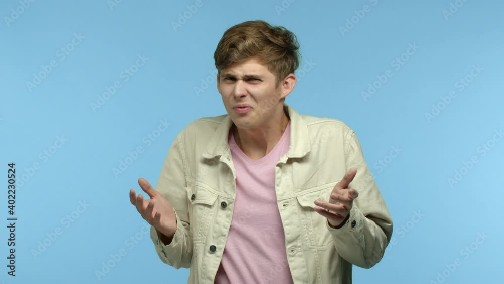 Slow motion of young man in casual clothes staring with cringe and disgust, frowning and grimacing as staring at something awful, shaking hands to decline and refuse, blue background Slow motion of young man in casual clothes staring with cringe and disgust, frowning and grimacing as staring at something awful, shaking hands to decline and refuse, blue background