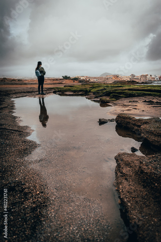 a girl with a blue backpack walking along a beach on a cloudy winter day