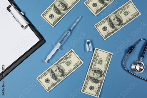 Stethoscope tablet for writing patients dollars syringe and vial with vaccine on blue background