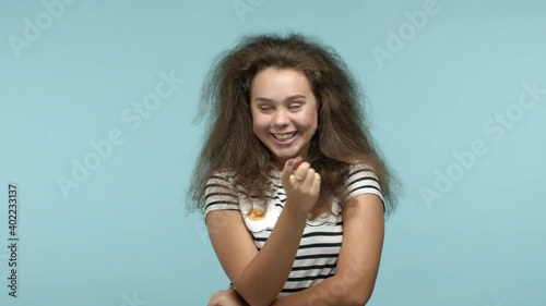Young seductive woman beckon you flirty with finger, asking to come closer and smiling, luring someone, standing over blue background in striped t-shirt