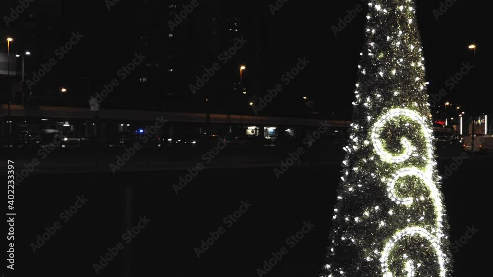 árbol de navidad alumbrado con luces  blancas  con fondo negro y coches en movimiento en las inmediaciones de un centro comercial situado en Bizkaia en horario nocturno