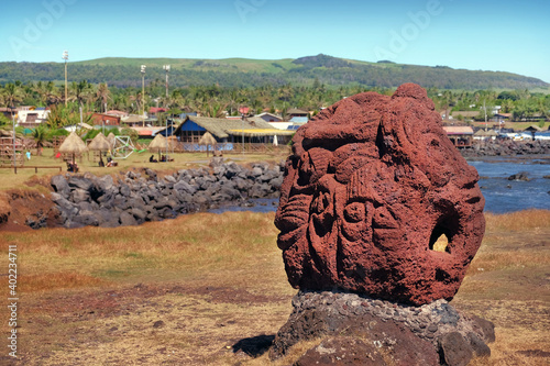 Carved figure in volcanic stone near the village of Hanga Roa, on Easer Island, against the ocean and a blue sky covered by white clouds. photo