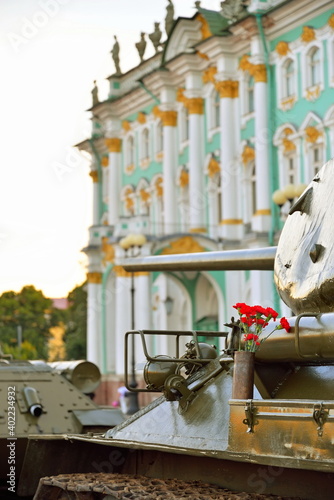Red carnations in a gun cartridge on the middle of the Soviet tank T-34-85 on the background of the Winter Palace