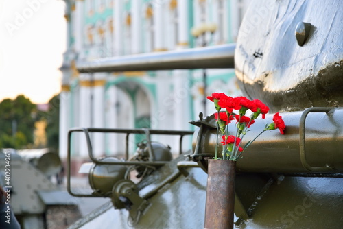 Red carnations in a gun shell closeup on the middle of the Soviet tank T-34-85 on the background of the Winter Palace