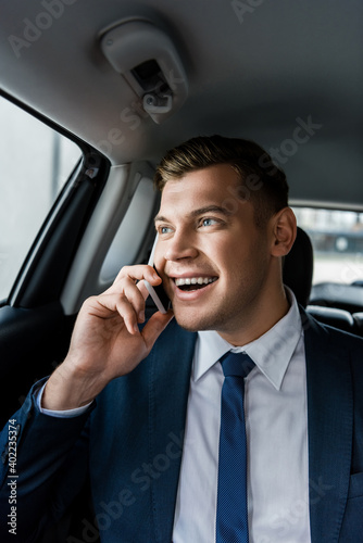 Young businessman smiling while talking on smartphone on back seat of auto. © LIGHTFIELD STUDIOS