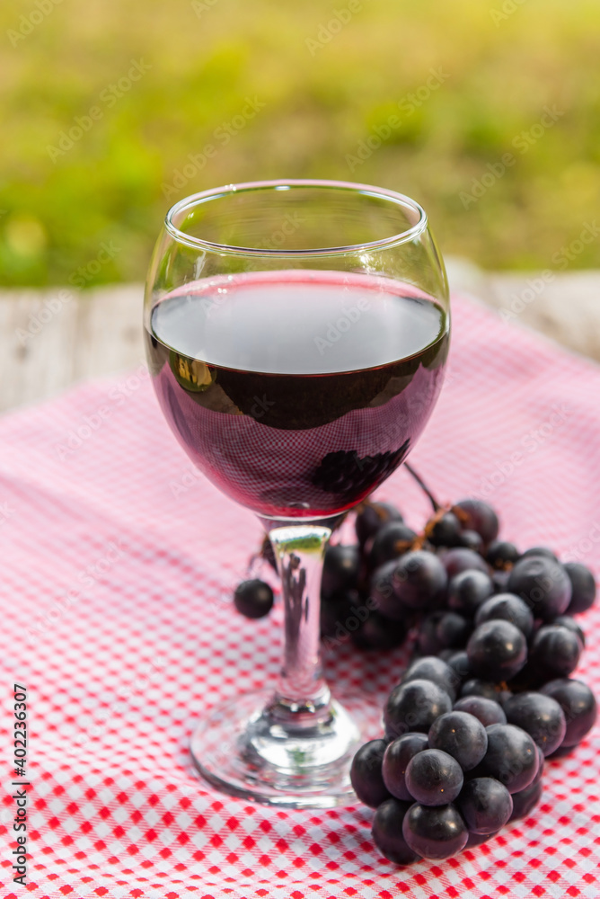 A glass of red wine with a bunch of grapes.