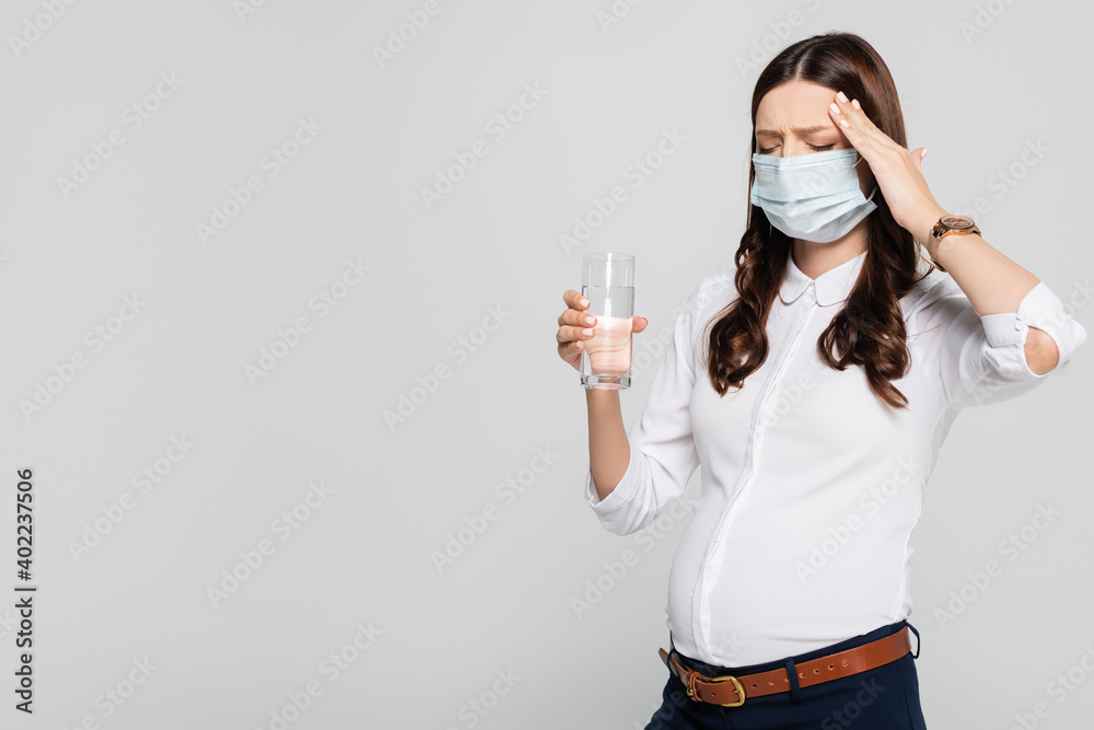pregnant businesswoman in medical mask with water having headache isolated on grey pregnant businesswoman in medical mask with water having headache isolated on grey