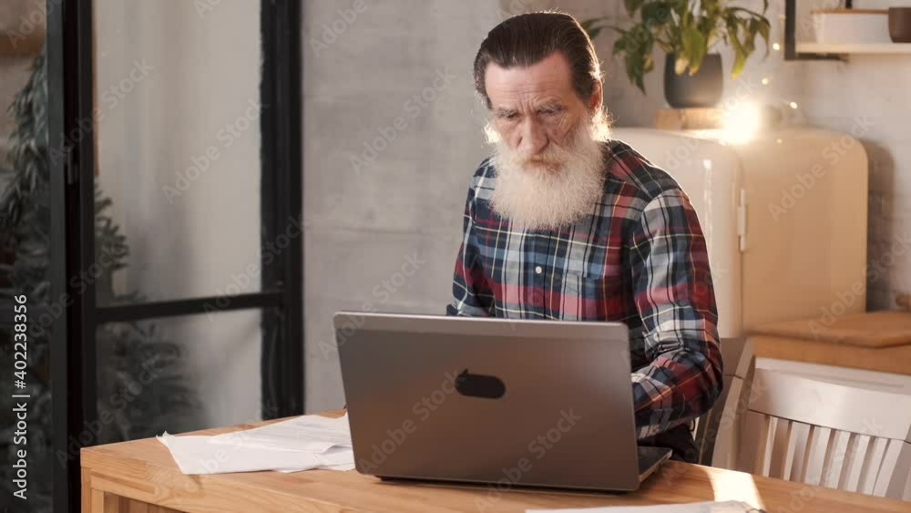 Senior man using his laptop and taking notes at home, close up. Contemporary lifestyle, old people and technology concept.