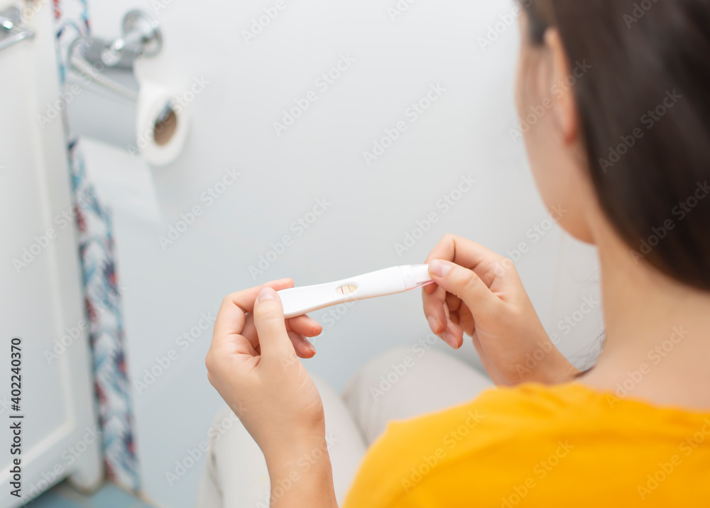 Closeup of young woman hold positive pregnancy test in bathroom ...