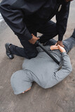 high angle view of african american policeman with truncheon frisking hooded offender lying on street.