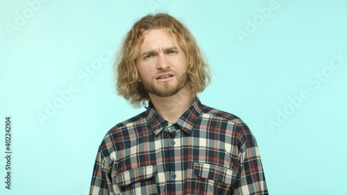 Slow motion of blond man with beard raising eyebrows surprised, hear something strange and looking confused, asking what and string questioned at camera, cant understand turquoise background