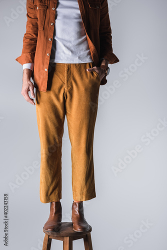 Cropped view of stylish man with hand in pocket standing on chair isolated on grey