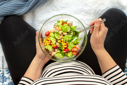 Cropped image of young hungry pregnant woman eating fresh tuna salad from glass bowl. Concept of healthy nutrition, vegetables and fish during pregnancy. Mother waiting baby. Omega 3 and vitamins.