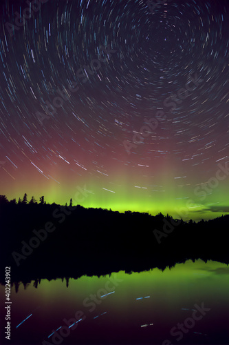 Star trail and Colorful green and purple Northern Lights (Aurora Borealis) night sky above a lake in Algonquin Park, Ontario, Canada