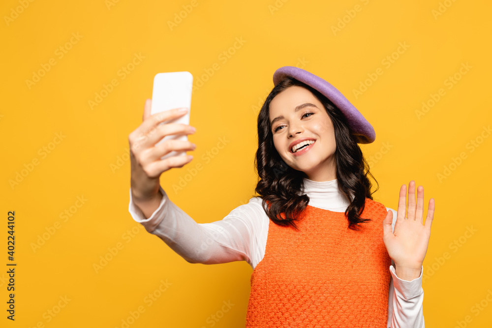 brunette woman with waving hand, wearing beret and taking selfie isolated on yellow brunette woman with waving hand, wearing beret and taking selfie isolated on yellow