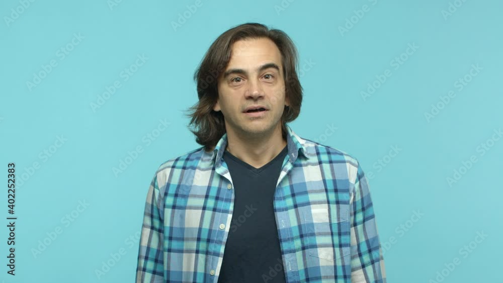 Slow motion of handsome middle-aged man with long hair, watching something with hopeful eyes, starting to rejoice and celebrating, laughing from happiness and triumph, blue background Slow motion of handsome middle-aged man with long hair, watching something with hopeful eyes, starting to rejoice and celebrating, laughing from happiness and triumph, blue background