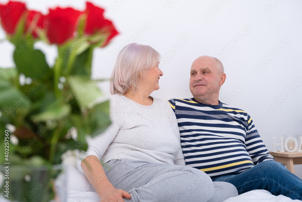 romantic senior couple hugging sitting on bed. bouquet of roses romantic senior couple hugging sitting on bed. bouquet of roses