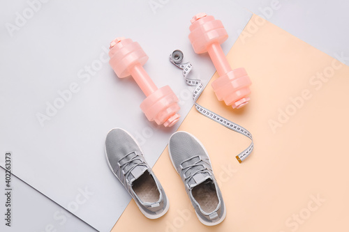 Dumbbells, measuring tape and sport shoes on color background © Pixel-Shot