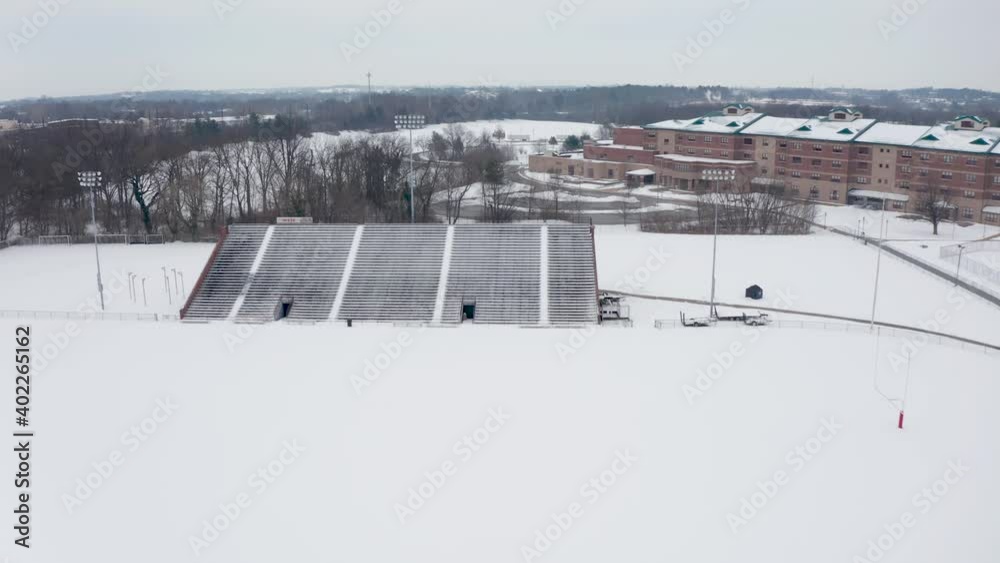 Aerial of school athletic fields and bleachers covered in winter snow. University college campus in United States of America during snowstorm. Aerial drone overhead view. Aerial of school athletic fields and bleachers covered in winter snow. University college campus in United States of America during snowstorm. Aerial drone overhead view.
