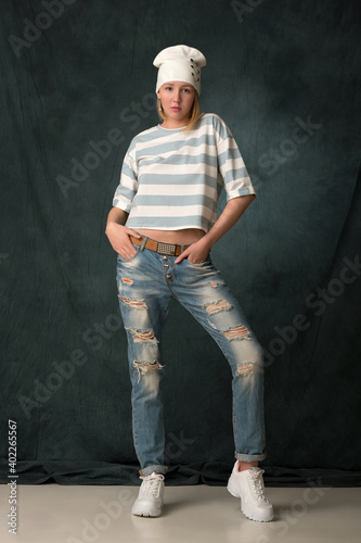 beautiful girl in jeans, a cap and a striped T-shirt posing on a gray background
