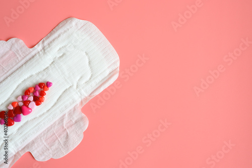 women's menstrual sanitary pad or napkin for normal profusion of secretions with red and pink beads in the shape of hearts as an imitation of blood on pink background
