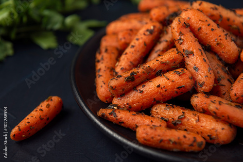 Black plate with small peeled pieces of cooked carrot and parsley on dark textured background