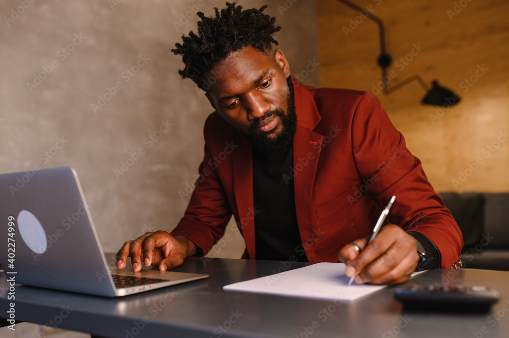 a focused black man in a suit is working on a laptop. Remote work from home a focused black man in a suit is working on a laptop. Remote work from home