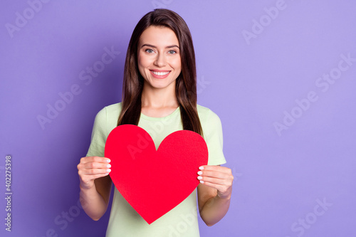 Photo portrait of girl wearing green t-shirt showing red paper heart symbol of love isolated on vivid purple color background