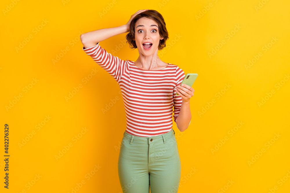 Portrait of nice person shocked hand on head open mouth hold smartphone isolated on yellow color background Portrait of nice person shocked hand on head open mouth hold smartphone isolated on yellow color background