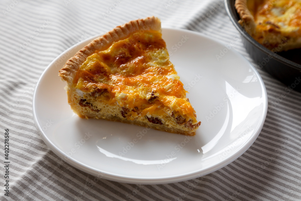 Homemade Bacon Quiche with Eggs and Cheddar Cheese on a white plate, side view.