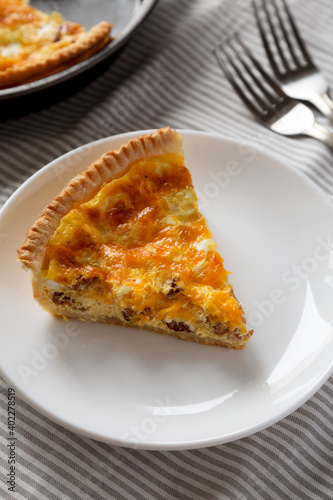 Homemade Bacon Quiche with Eggs and Cheddar Cheese on a white plate, side view.