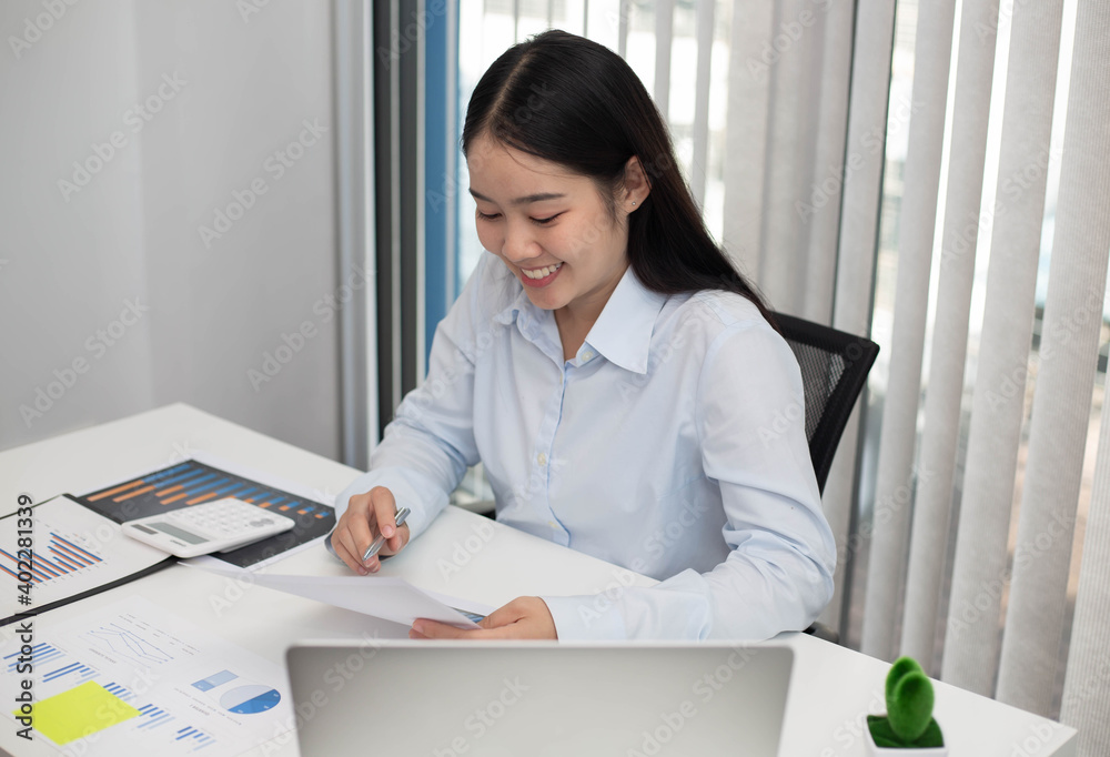 Portrait of businesswoman with laptop writes on a document and check graph at her office Portrait of businesswoman with laptop writes on a document and check graph at her office