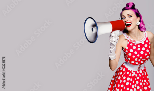 Purple head fashionable trendy woman using megaphone, shouting something. Pin up girl in red polka dot dress. Retro vintage studio concept. Grey color background. Copy space place for text.