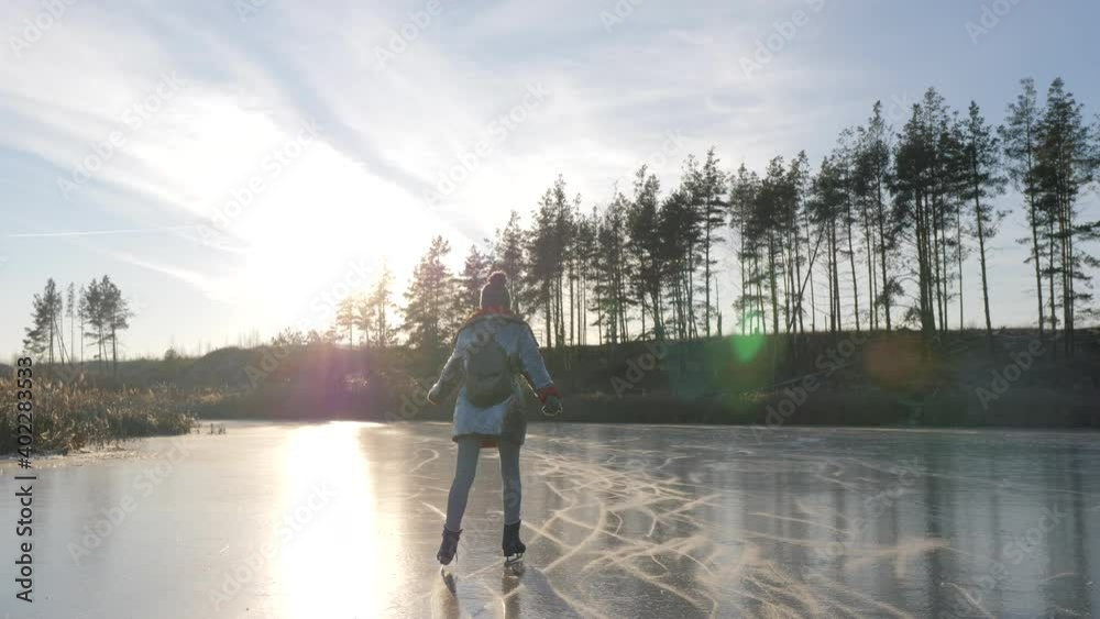 Young girl in silver jacket and backpack is skating on frozen lake. Woman rides to meet the sun on ice. Concept: dream and inspiration. Young girl in silver jacket and backpack is skating on frozen lake. Woman rides to meet the sun on ice. Concept: dream and inspiration.