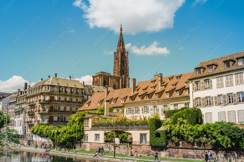 Scenic view of beautiful houses at a river front and the bell tower of the Strasbourg Cathedral in the background.